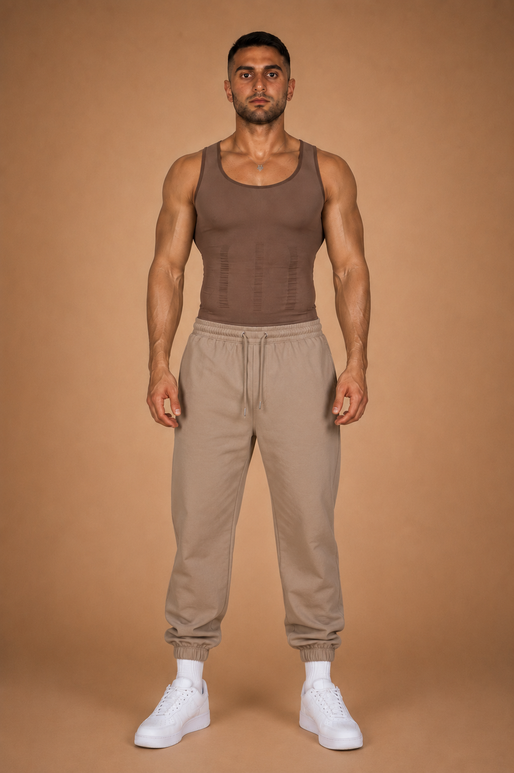 the cinch — brown seamless compression tank worn with sand joggers, full-length front view against warm backdrop