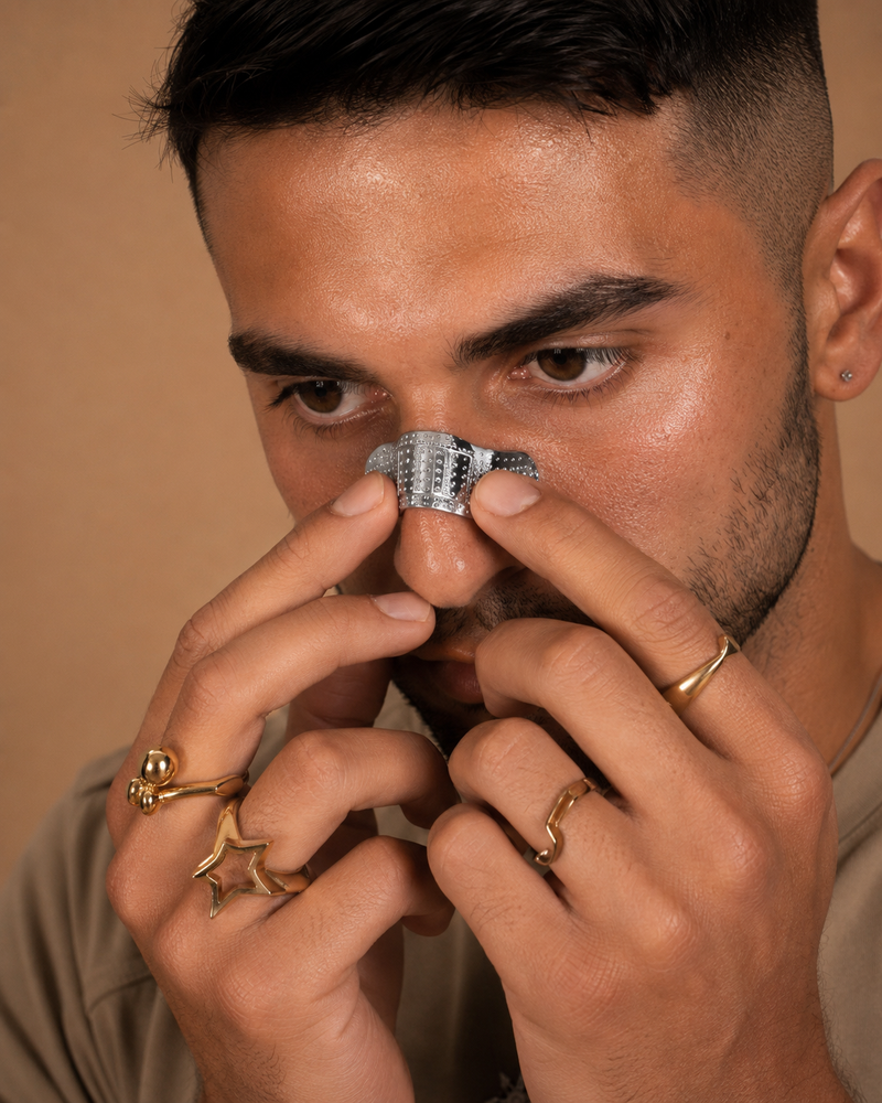 the bridge, studded alloy nose cuff worn across the nose bridge, front portrait on warm backdrop