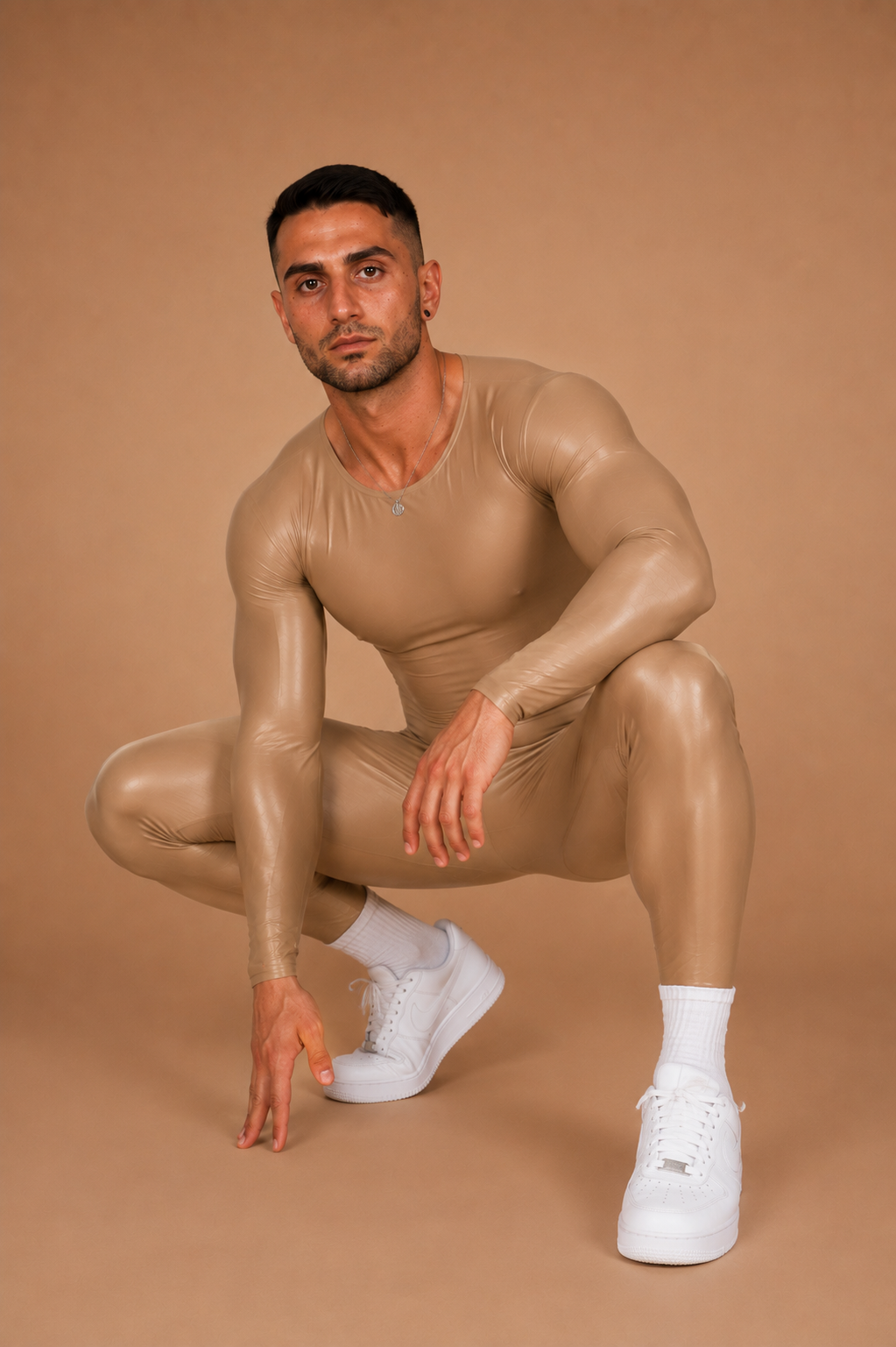 the second skin — crouched pose showing full-body fit and sheen, warm sand backdrop